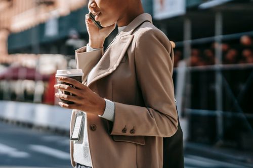 Free Side view crop positive African American female in formal outfit standing on street with takeaway coffee and talking on mobile phone Stock Photo