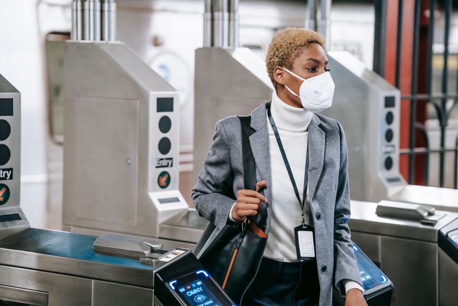 Calm attractive African American female in stylish formal wear and protective mask passing through turnstile gates in underground station