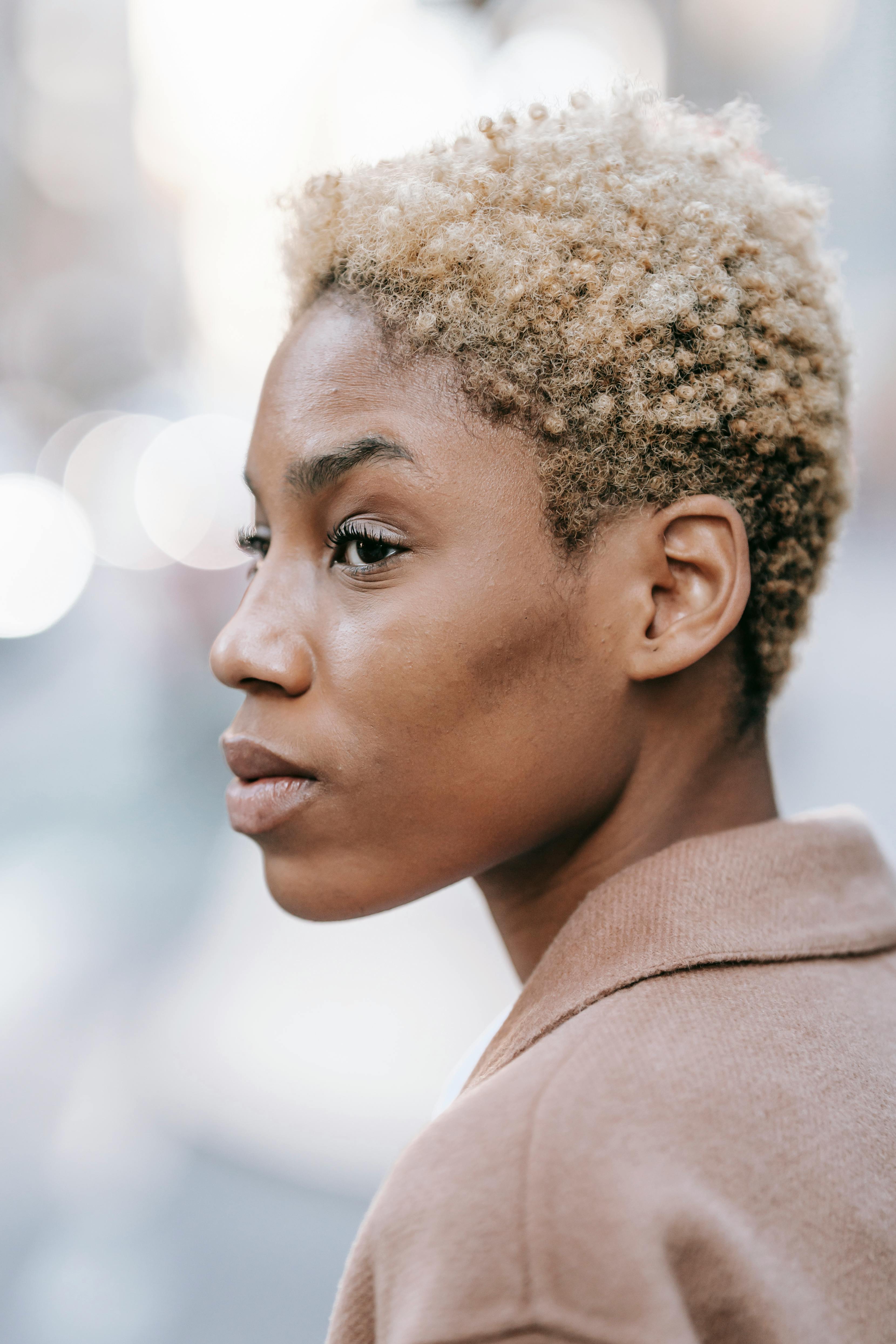 Profile of a young woman with short curly hair looking away in a city street.