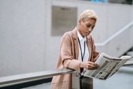 Focused black businesswoman reading newspaper on street