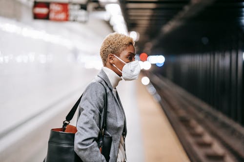 Pensive black woman in mask standing on railway platform