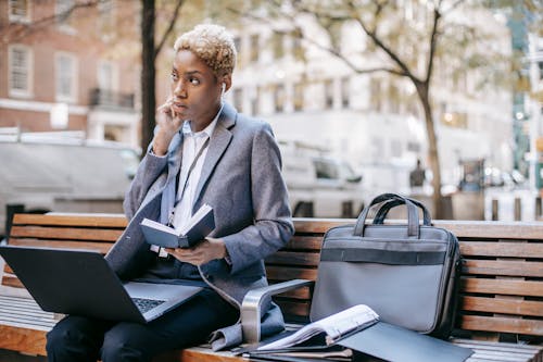 Focused black businesswoman working on laptop on bench in park