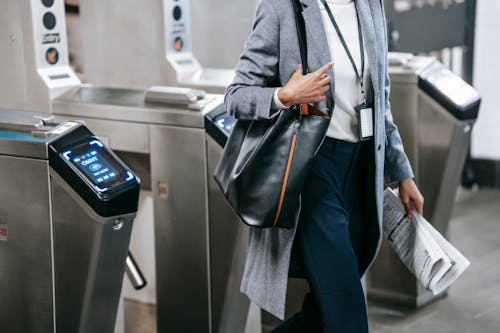 Crop anonymous African American female in formal clothes with newspaper passing through turnstile gates in modern underground station