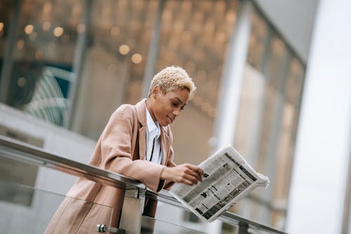 Content black woman reading newspaper outside modern business center
