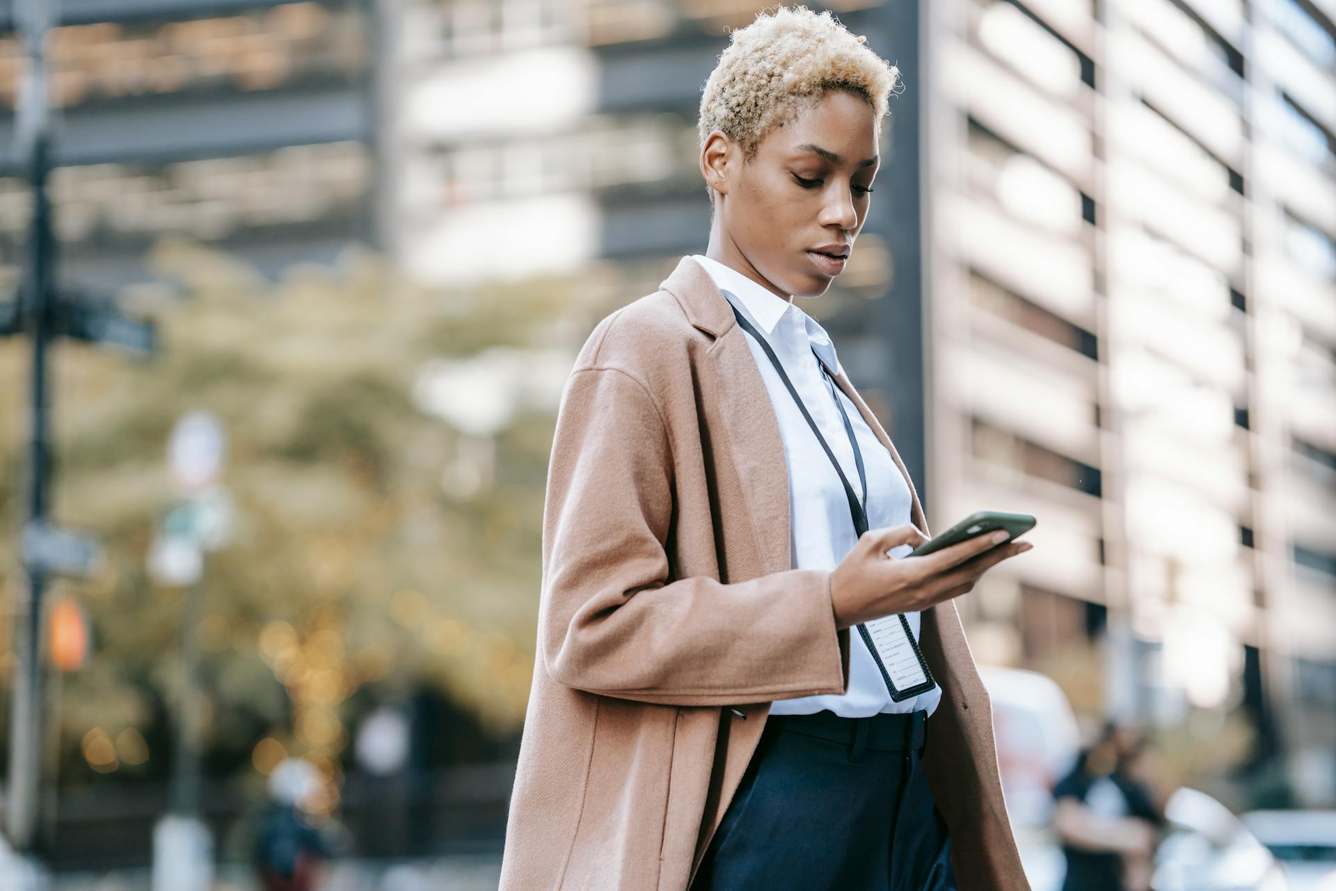 Focused black businesswoman browsing smartphone on urban street