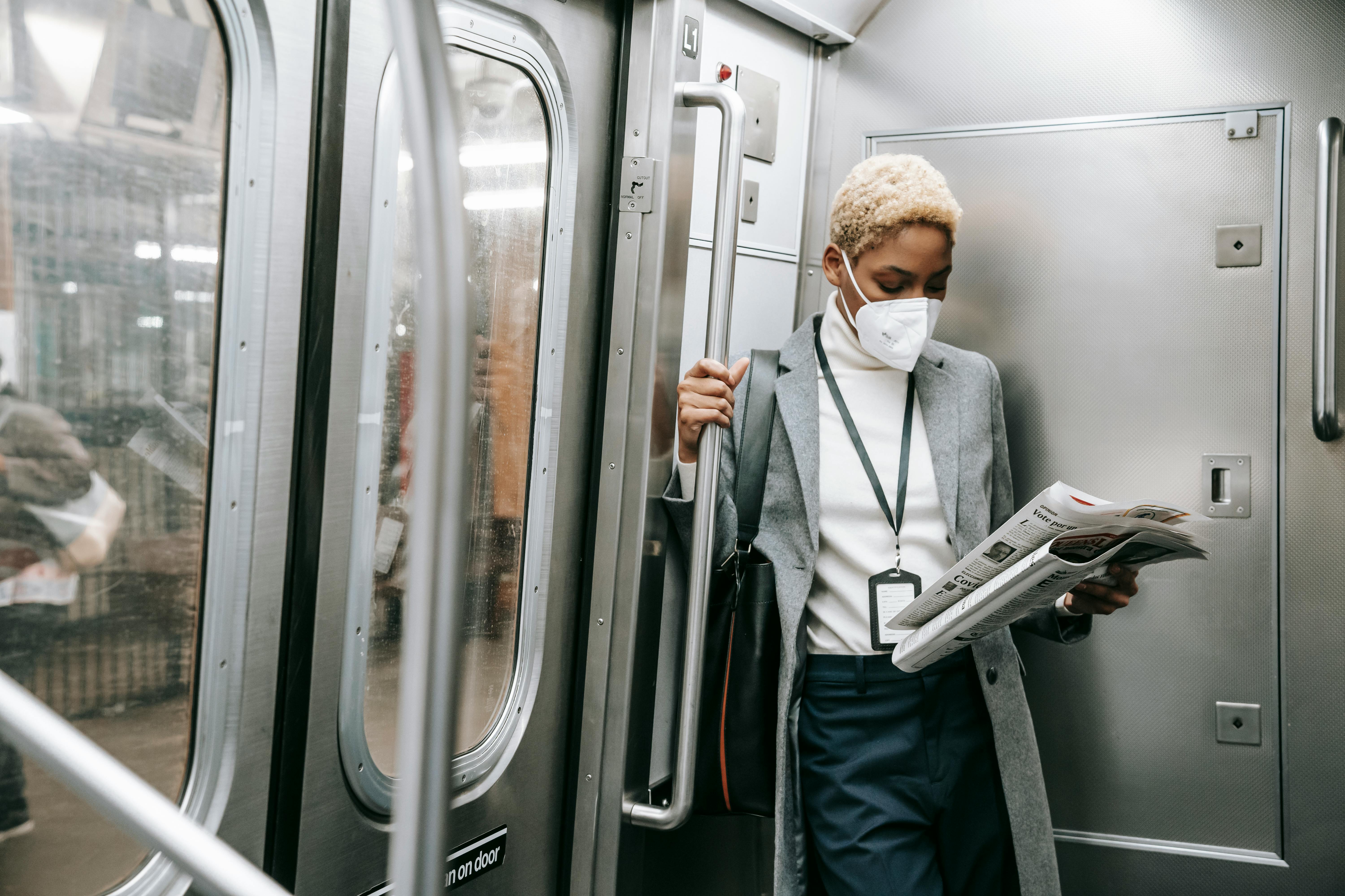 focused black woman in mask reading newspaper in metro train