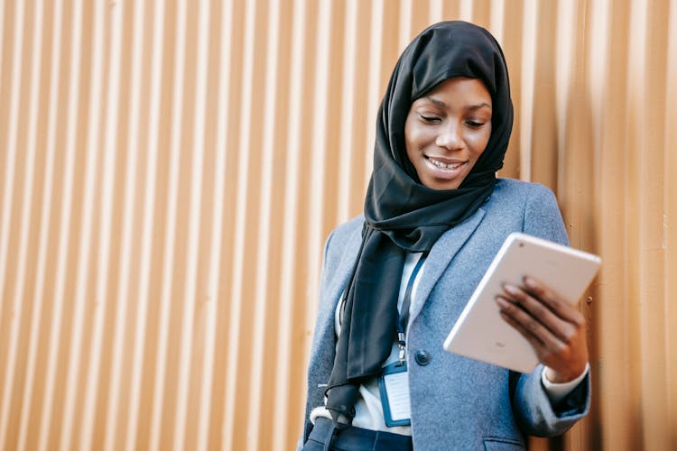 Smiling Muslim Black Woman Using Tablet Against Brown Wall