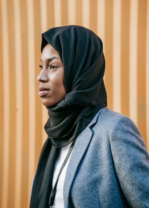 Content Muslim black woman in hijab standing against brown wall