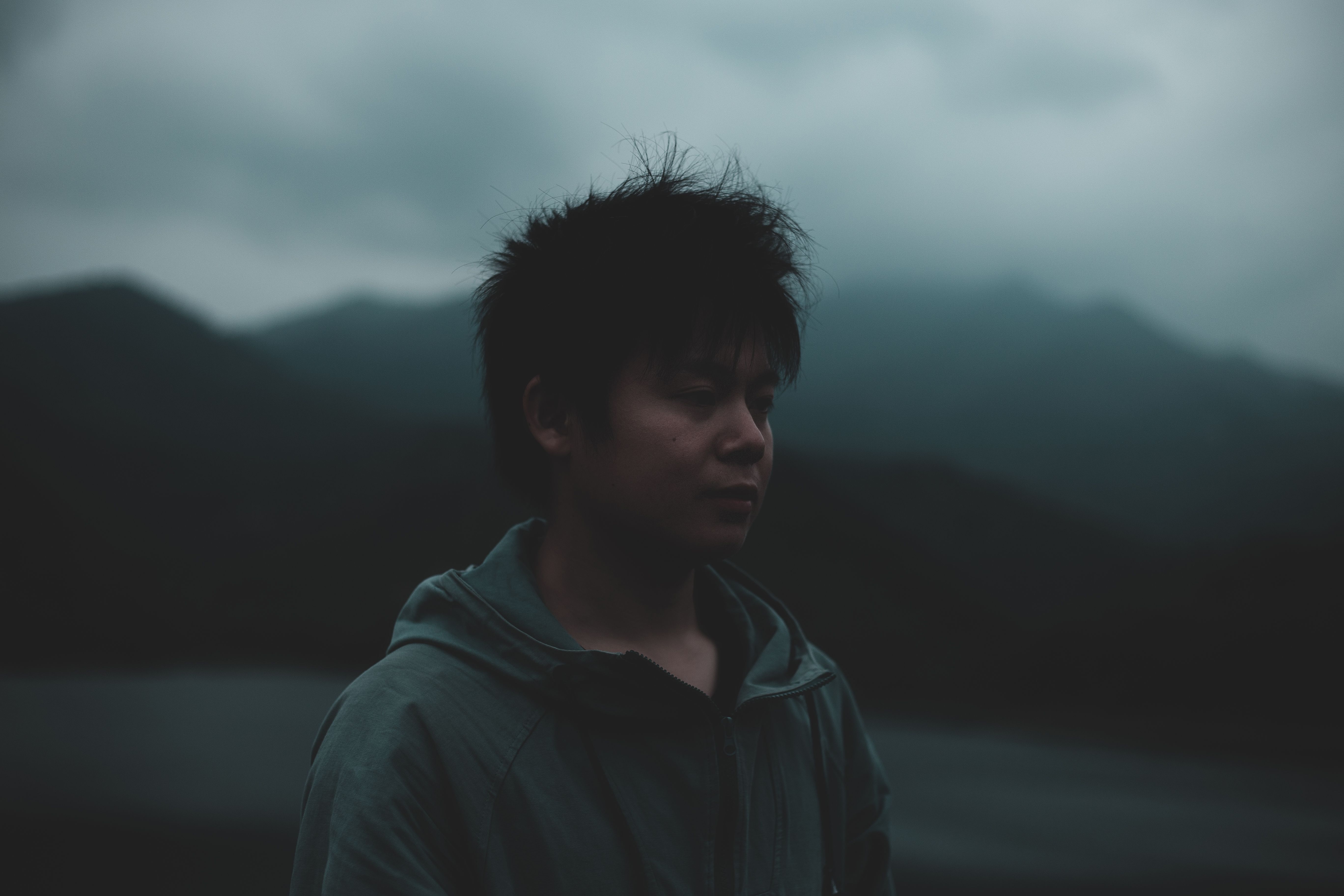 A contemplative young man stands against a misty mountainous background, evoking a sense of introspection.