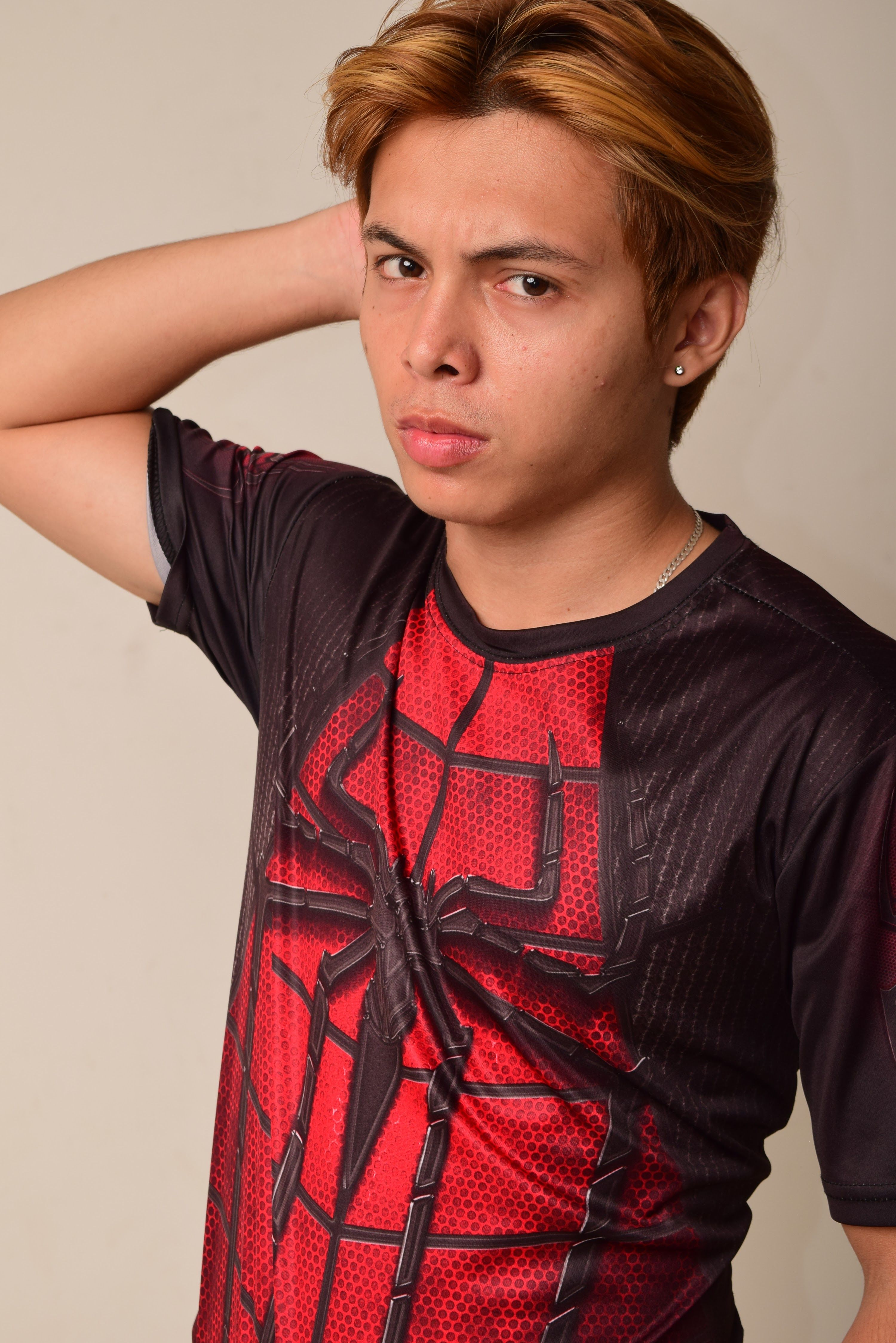 Young man posing with a serious expression wearing a Spiderman-themed shirt against a neutral background.