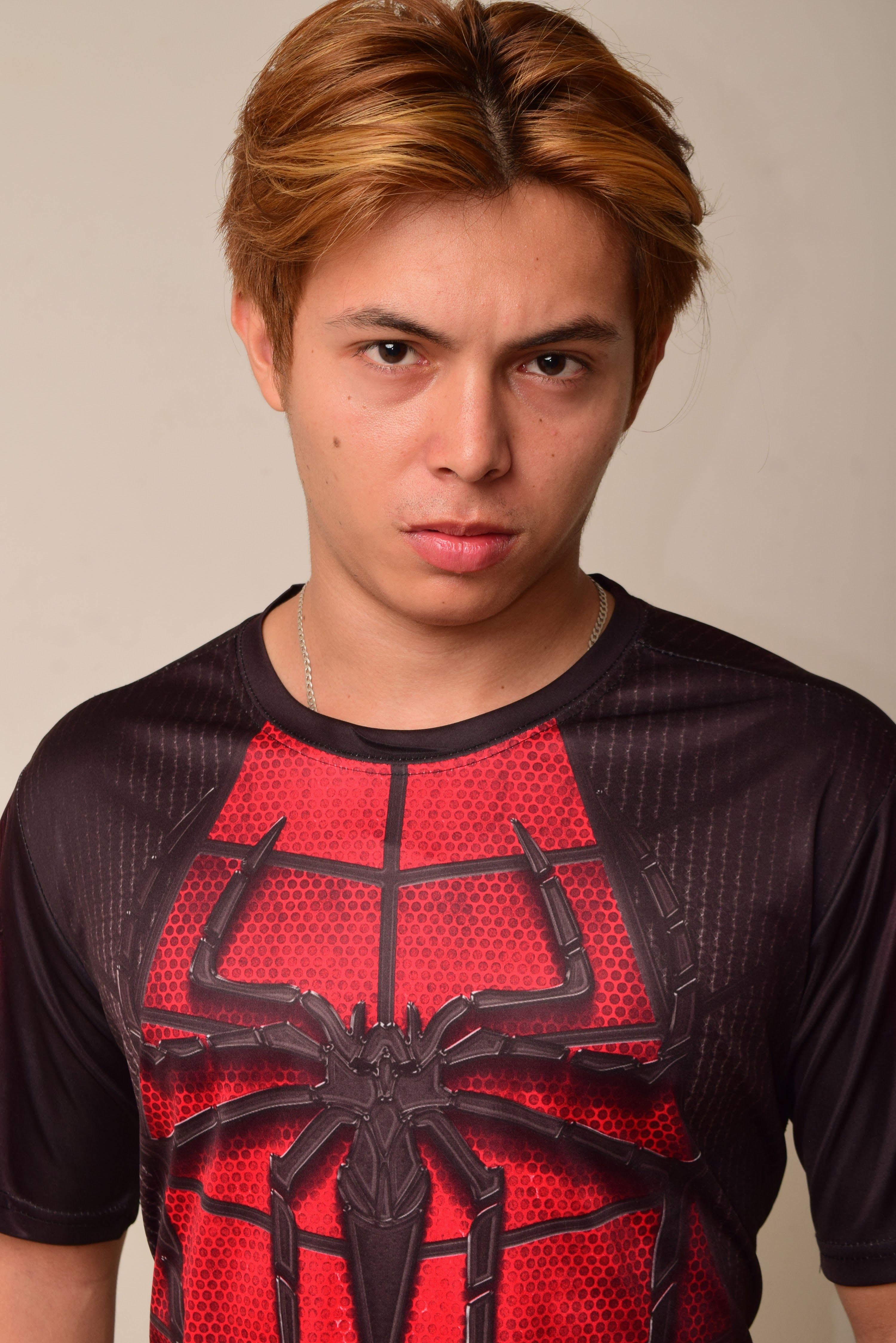 Close-up portrait of a young man wearing a Spiderman themed shirt with a serious expression.