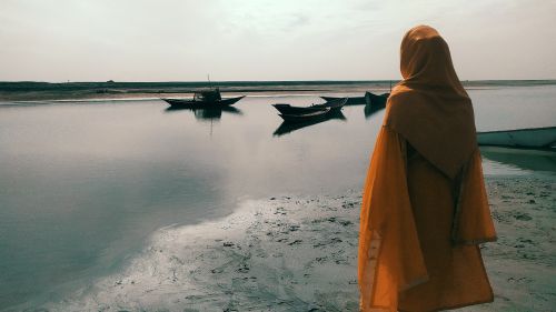 Free A solitary woman in a hijab gazes over a peaceful river with boats in Bangladesh. Stock Photo