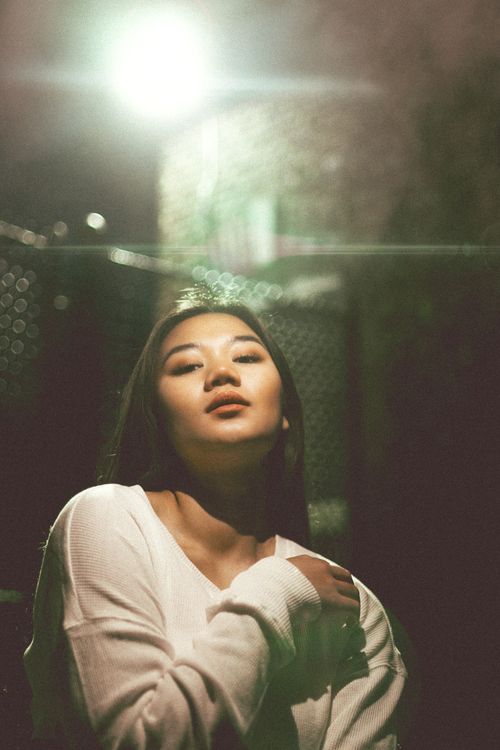Free Calm Asian female with dark hair in casual clothes standing on street against metal fence and looking at camera Stock Photo