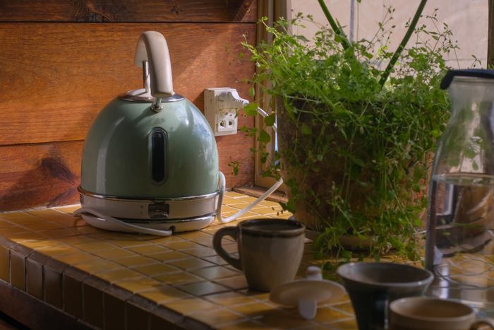 Kettle, mugs and a plant on a kitchen counter — photo by Duong Nhan on Pexels