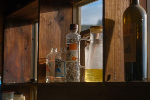 Variety of bottles on a wooden shelf illuminated by sunlight, creating a warm rustic feel.