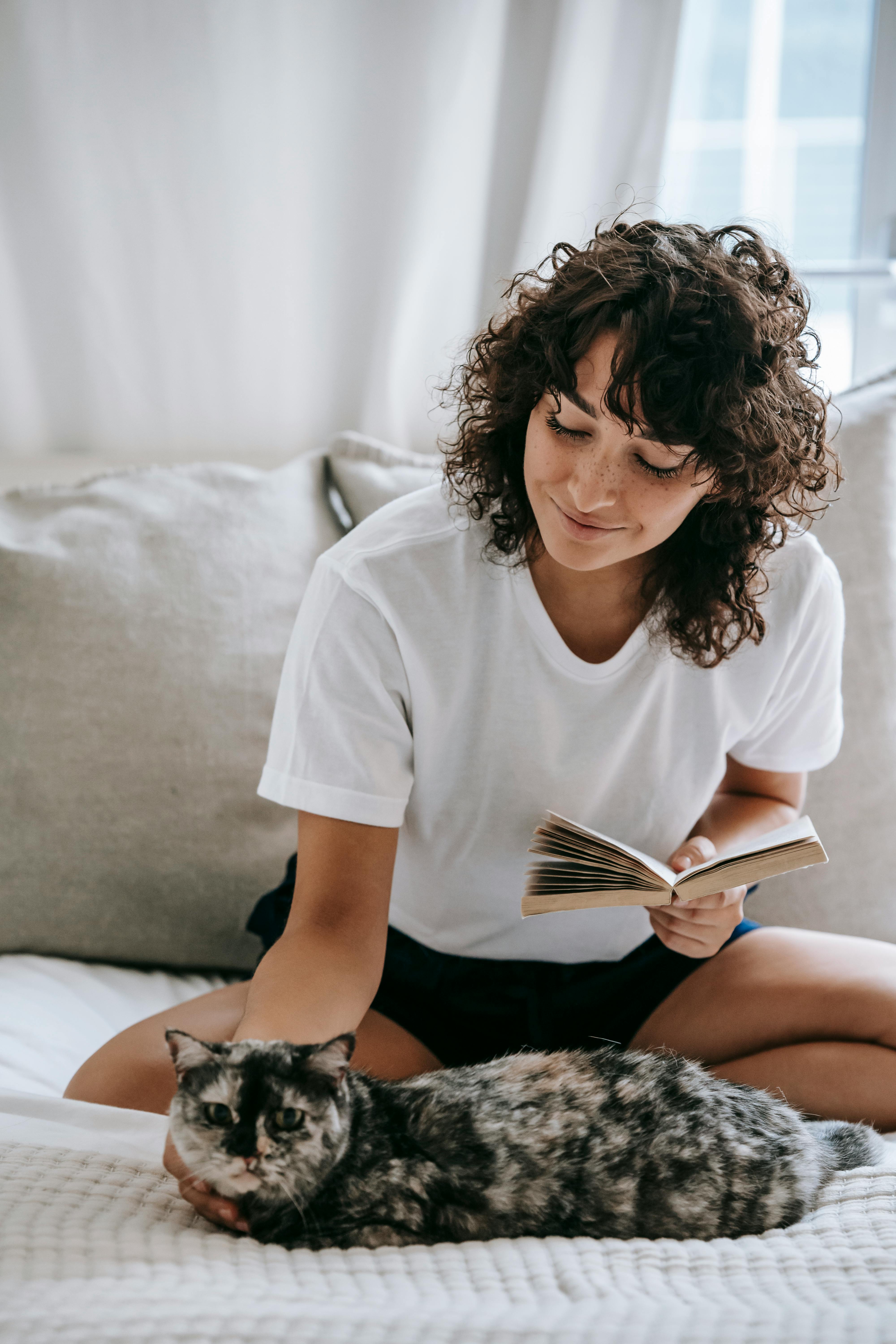 Smiling woman with book sitting on bed with cute cat