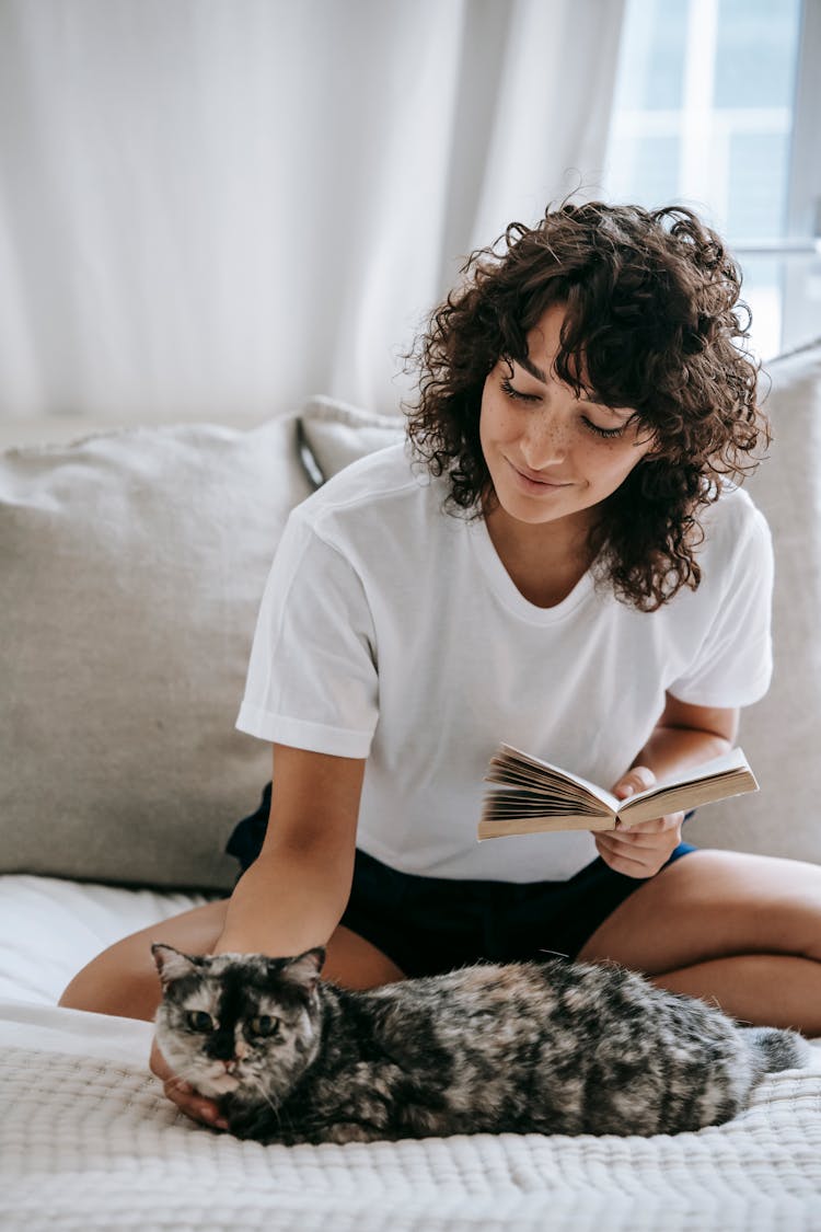 Smiling Woman With Book Sitting On Bed With Cute Cat