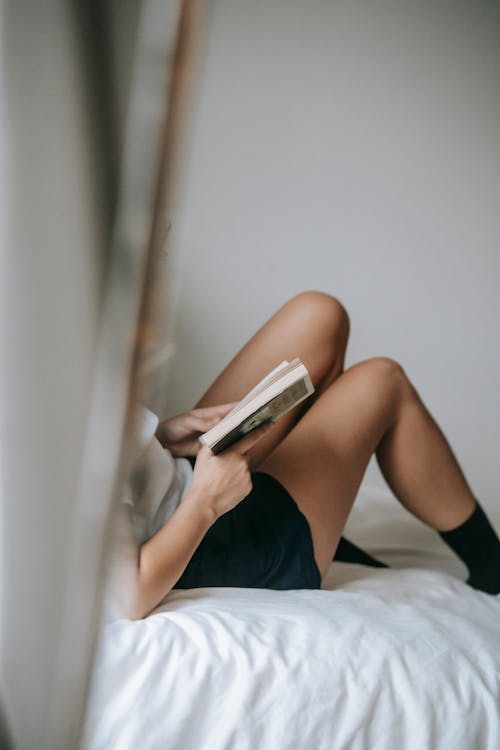 Crop unrecognizable woman reading book on cozy bed