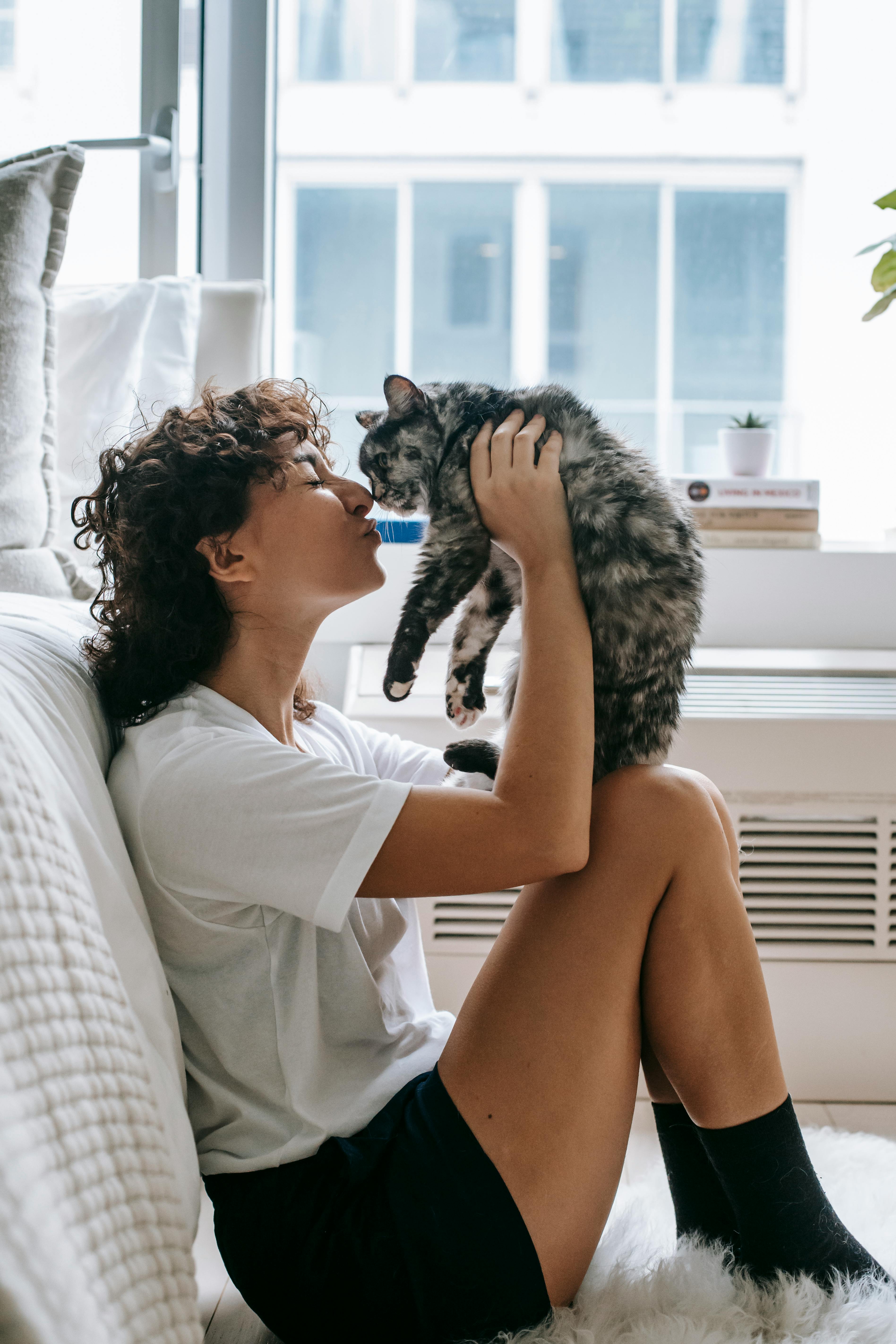 charming woman kissing cute cat in bedroom