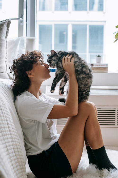 Charming woman kissing cute cat in bedroom