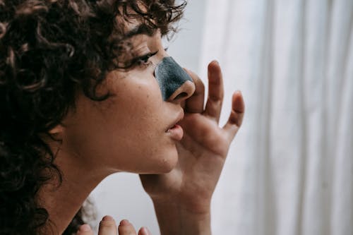 Side view of crop curly woman applying blackhead removing strip on nose standing in bathroom