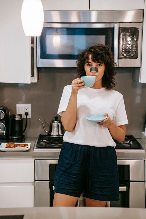 Free Charming curly brunette in cozy home wear and nose strip sipping hot drink in light kitchen looking at camera Stock Photo