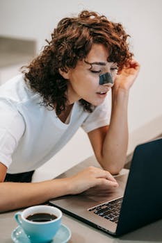 High angle of female with blackhead strip on nose using netbook while having coffee at home