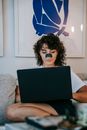 Calm young woman with skin care mask on nose relaxing on couch with netbook