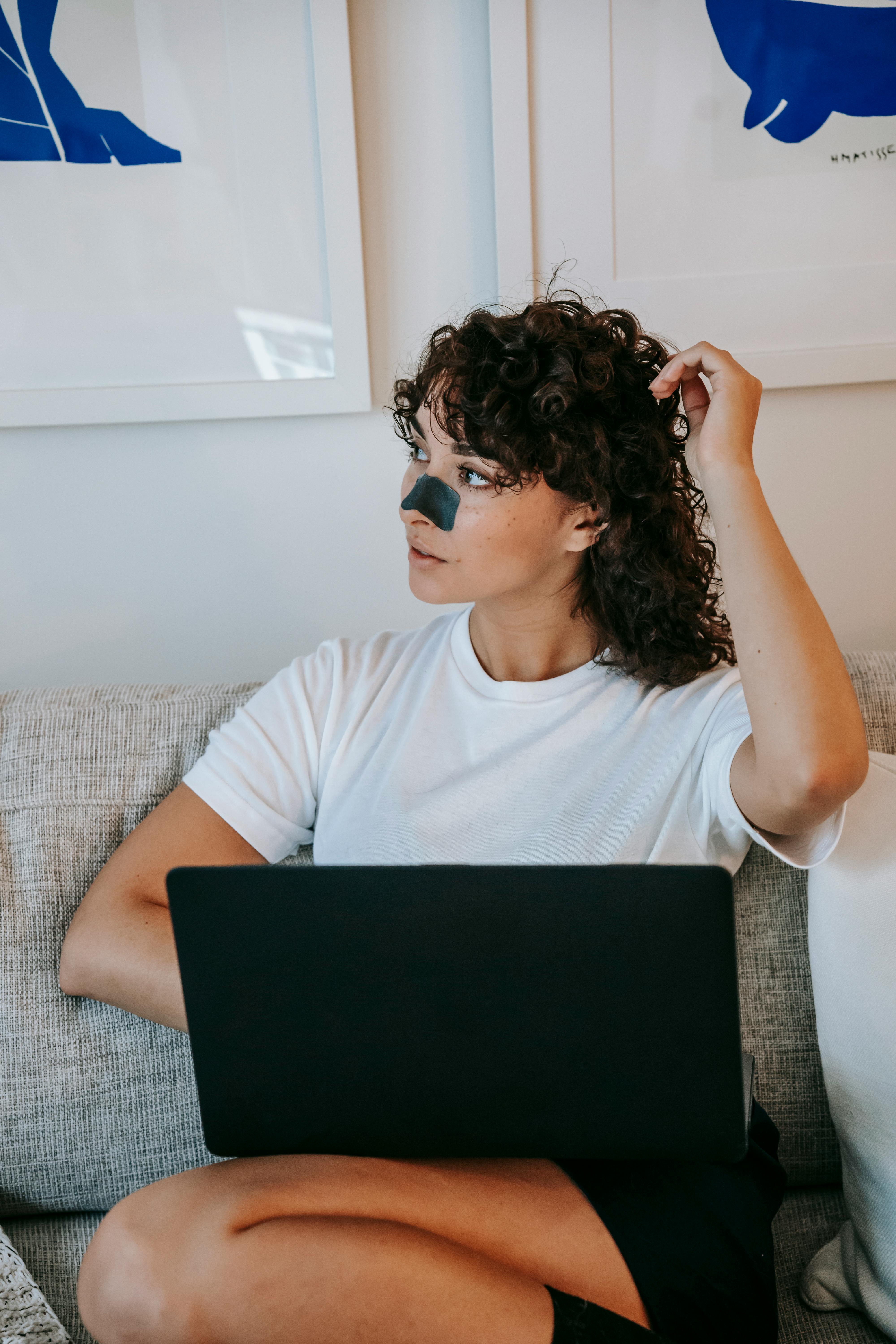 relaxed young female with nose patch relaxing on couch with laptop