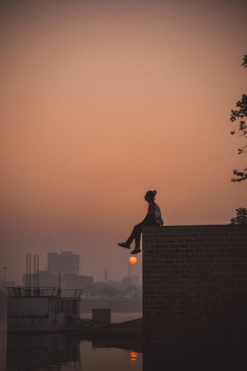 Free Man Sitting on Edge of Brick Wall During Sunset Stock Photo