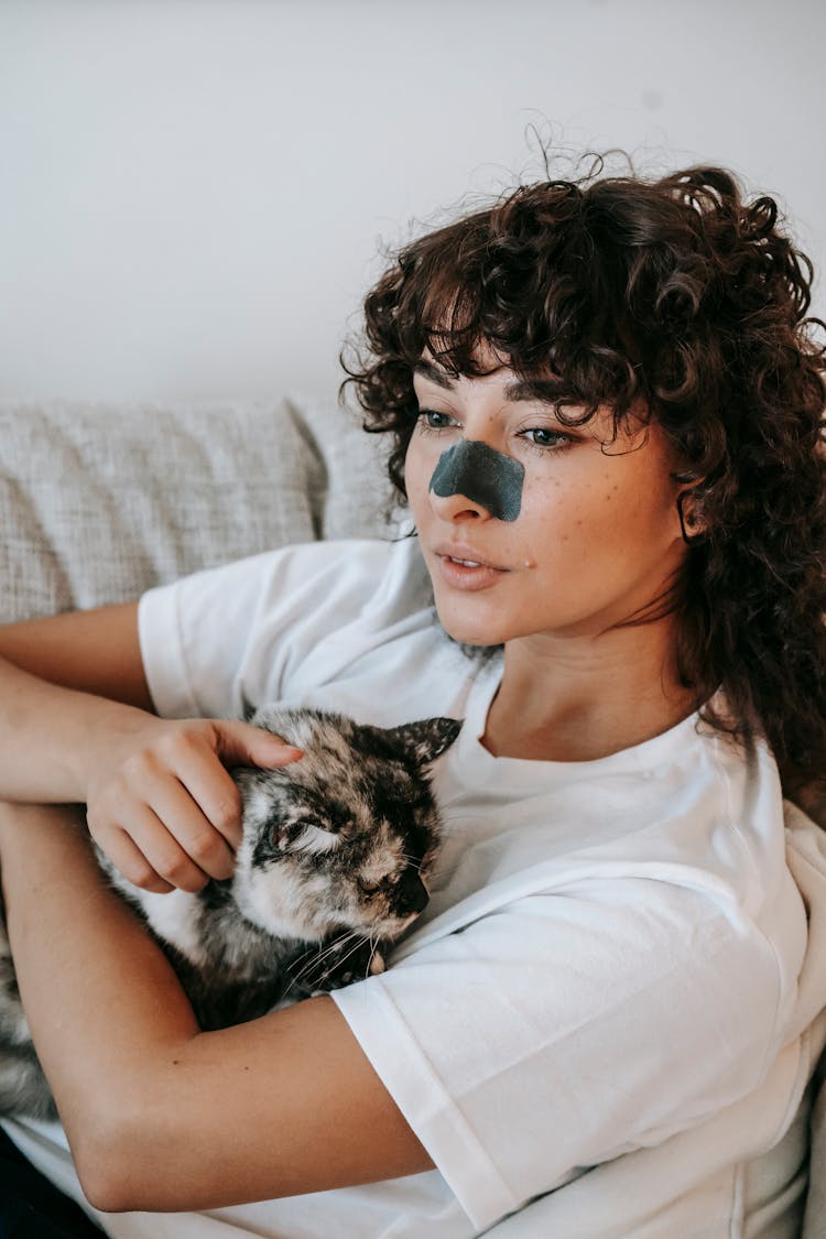 Young Female Owner Hugging Cat While Resting On Sofa During Skin Care Procedure