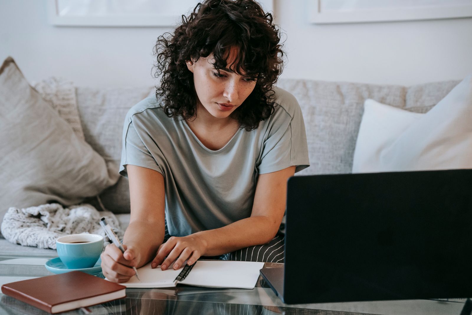 Student studying at home on a laptop while writing notes for exam preparation