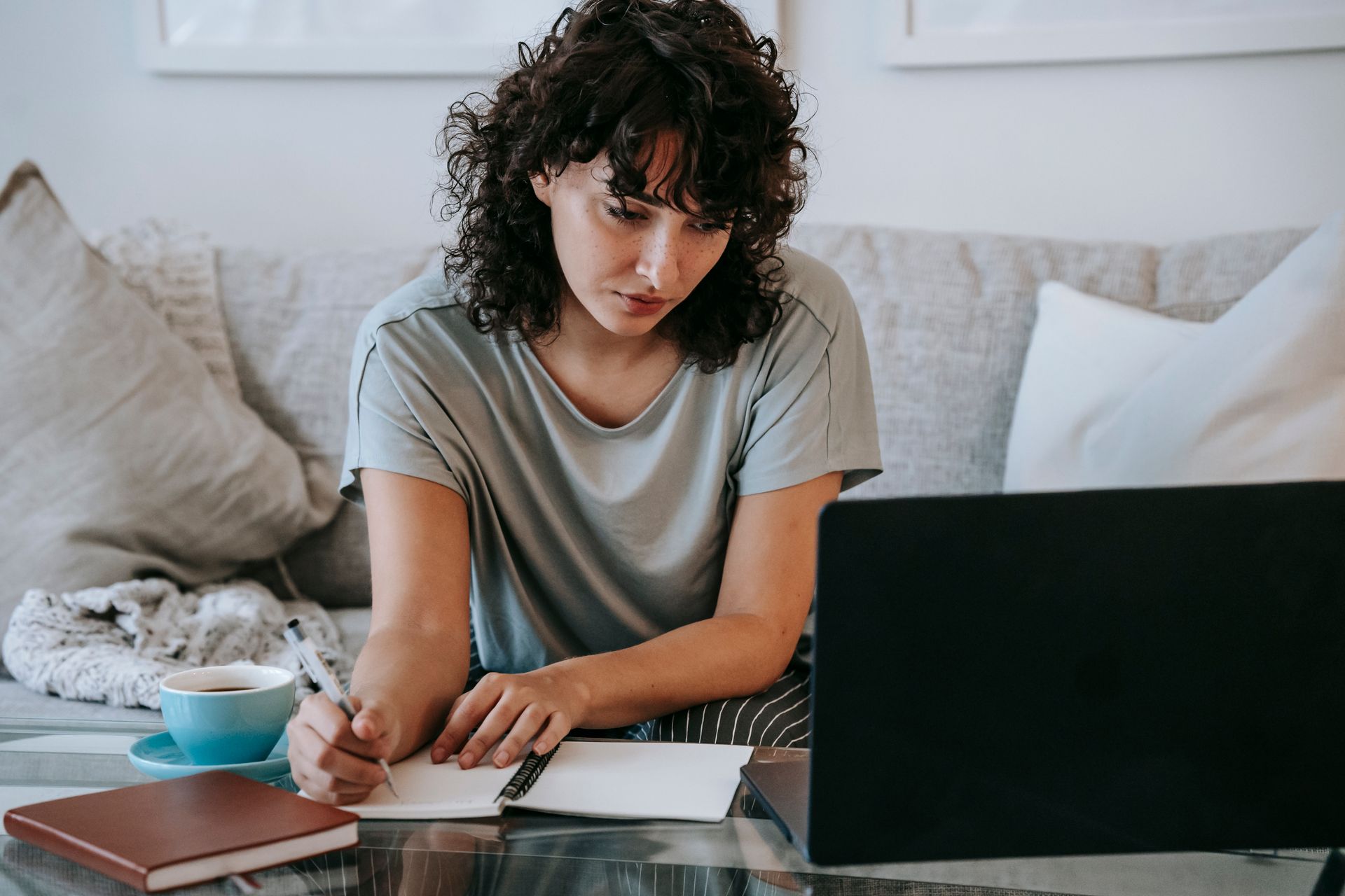 Serious young lady writing in notebook during online studies on laptop at home