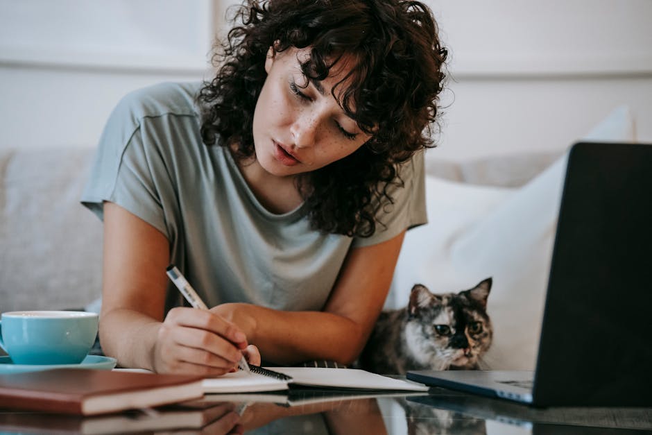 Focused young female student doing homework using netbook sitting near cute cat