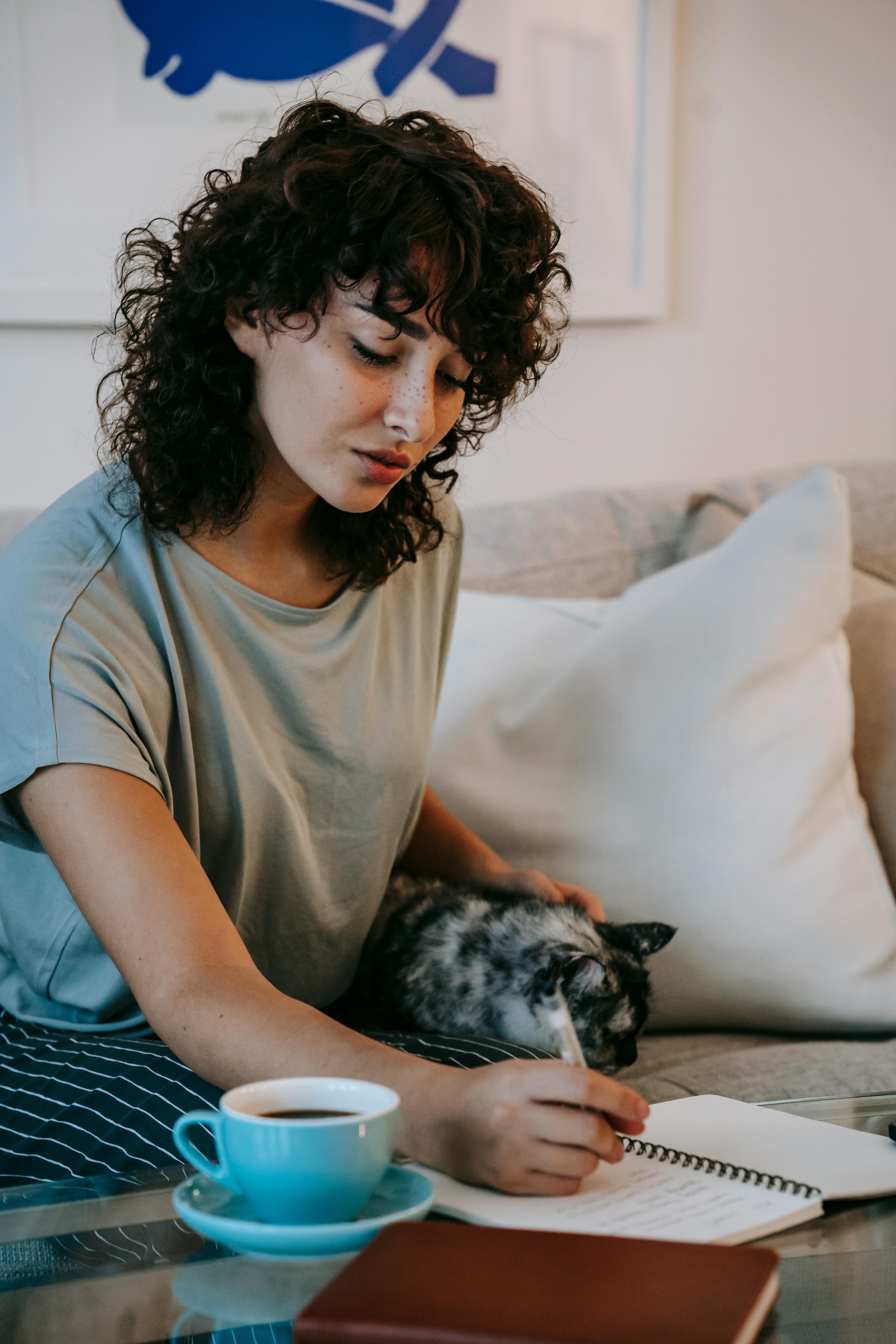 young woman caressing cat and writing in notebook during remote work at home