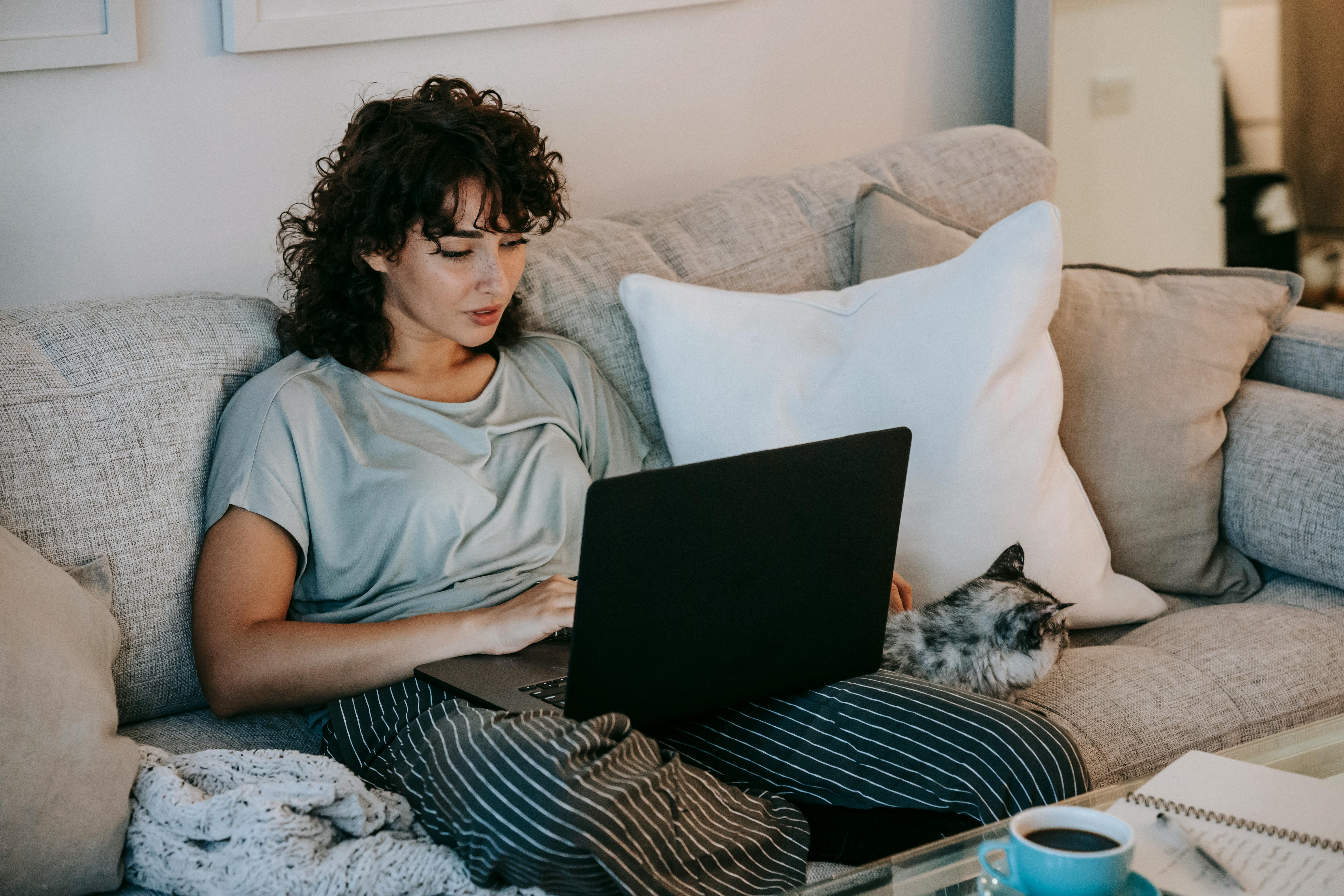 relaxed female watching movie on netbook and caressing cat on sofa