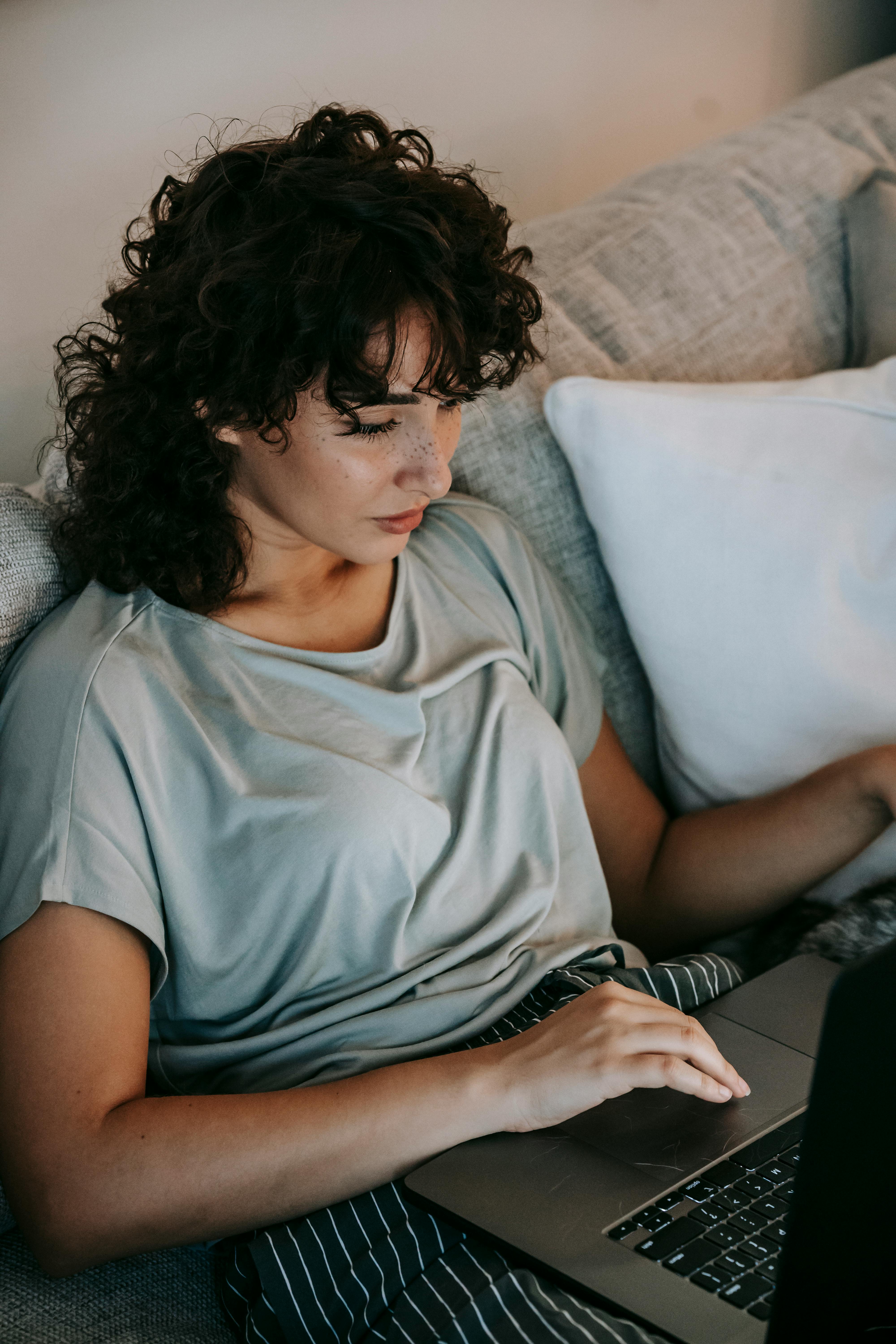 young ethnic lady working on netbook sitting on couch at home