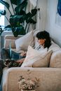 Side view of young ethnic female owner with dark curly hair relaxing on sofa with cute cat and watching interesting film on laptop