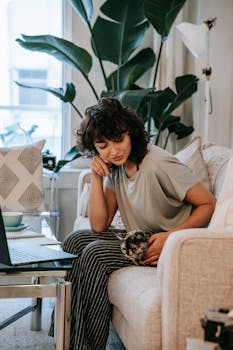 A young woman studying at home with her pet cat on a cozy sofa, using a laptop.