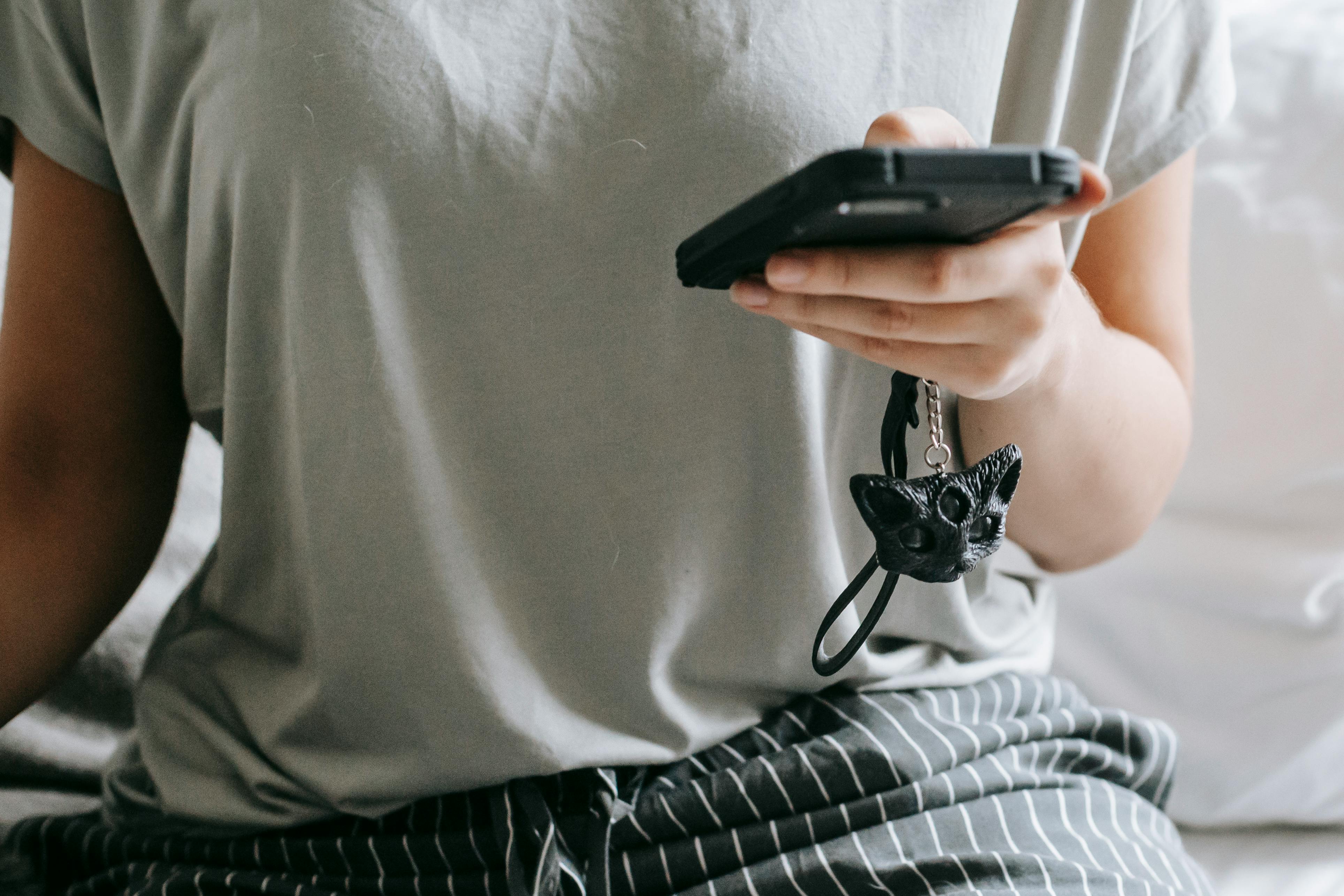 unrecognizable woman messaging on smartphone while sitting on bed at home