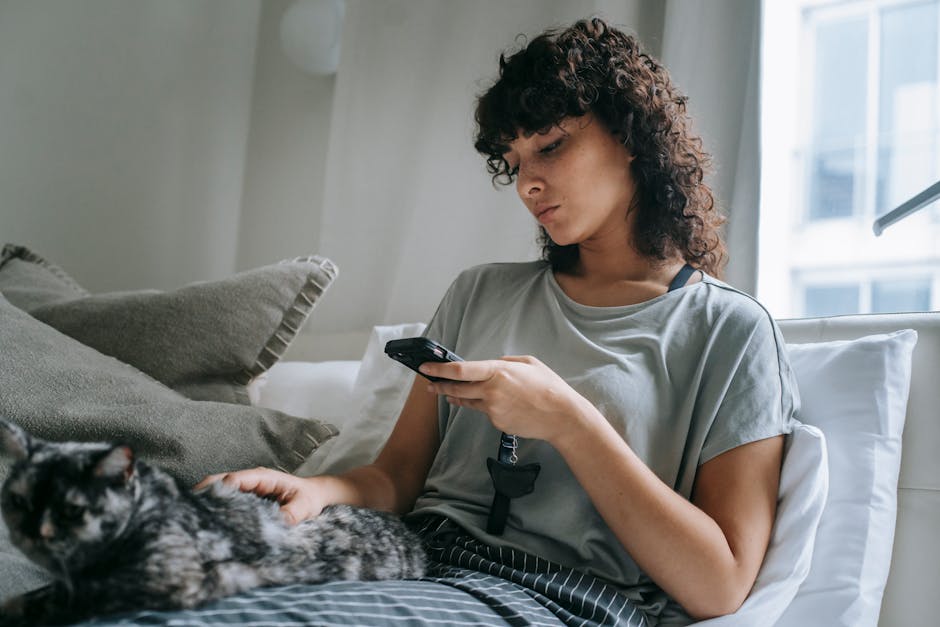 Thoughtful young ethnic female reading message and stroking cat on bed