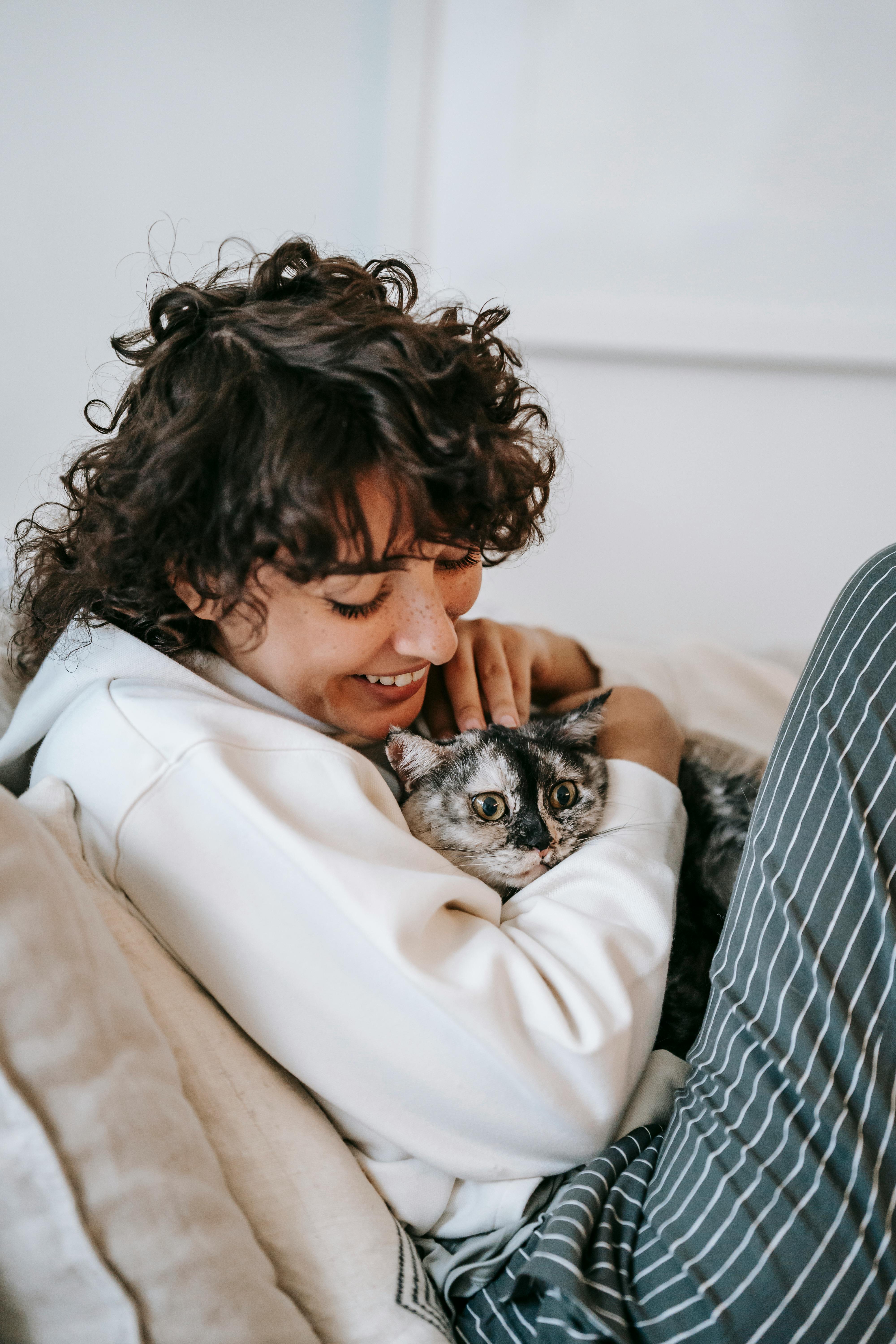 Cheerful woman cuddling cat on couch in house