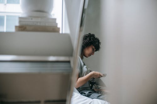 Free Side view of crop female text messaging on cellphone while resting near pile of books in house Stock Photo