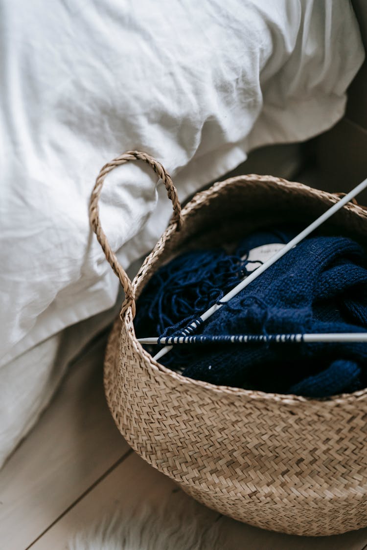 Woolen Fabric With Knitting Needles In Wicker Basket At Home