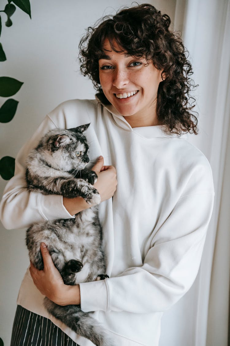 Smiling Woman Embracing Domestic Cat At Home