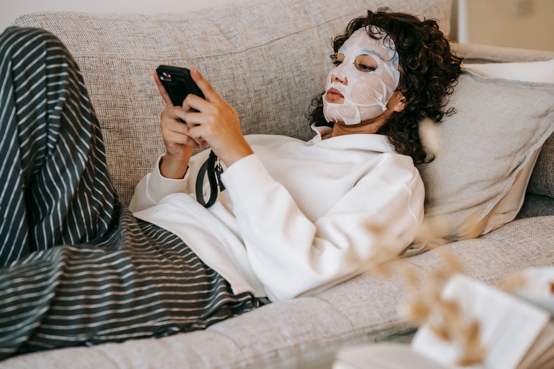 Free Focused woman with cosmetic mask browsing phone Stock Photo