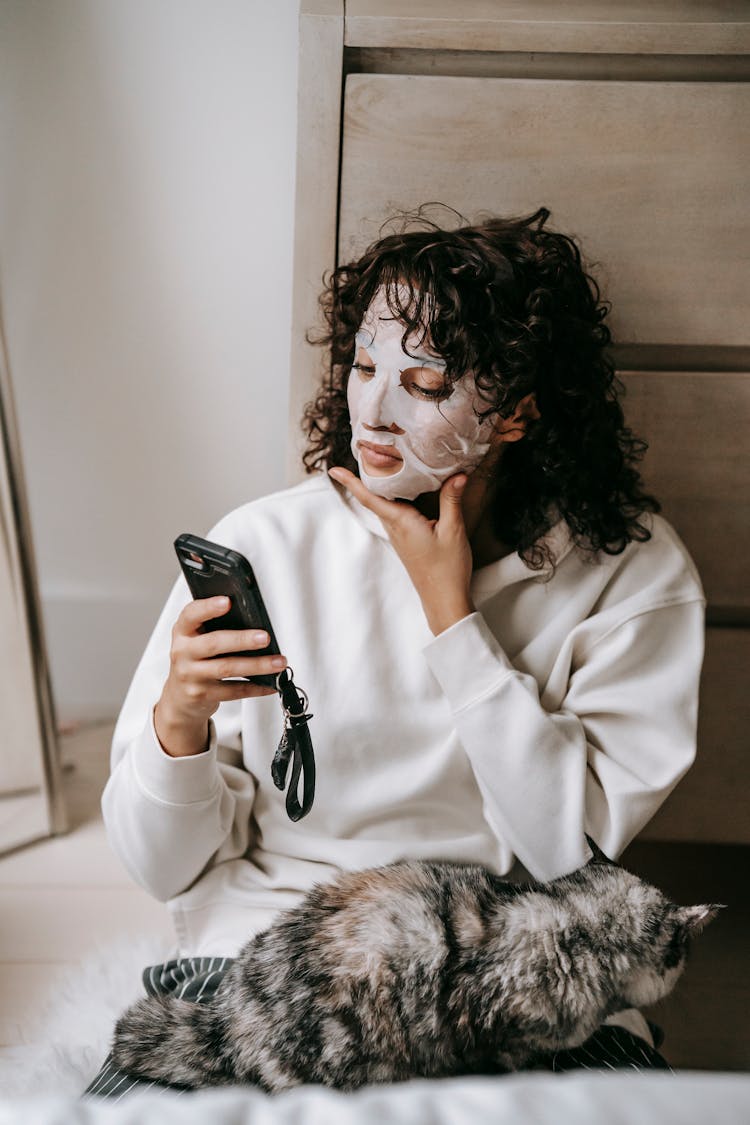 Concentrated Woman In Sheet Mask With Cat Surfing Smartphone