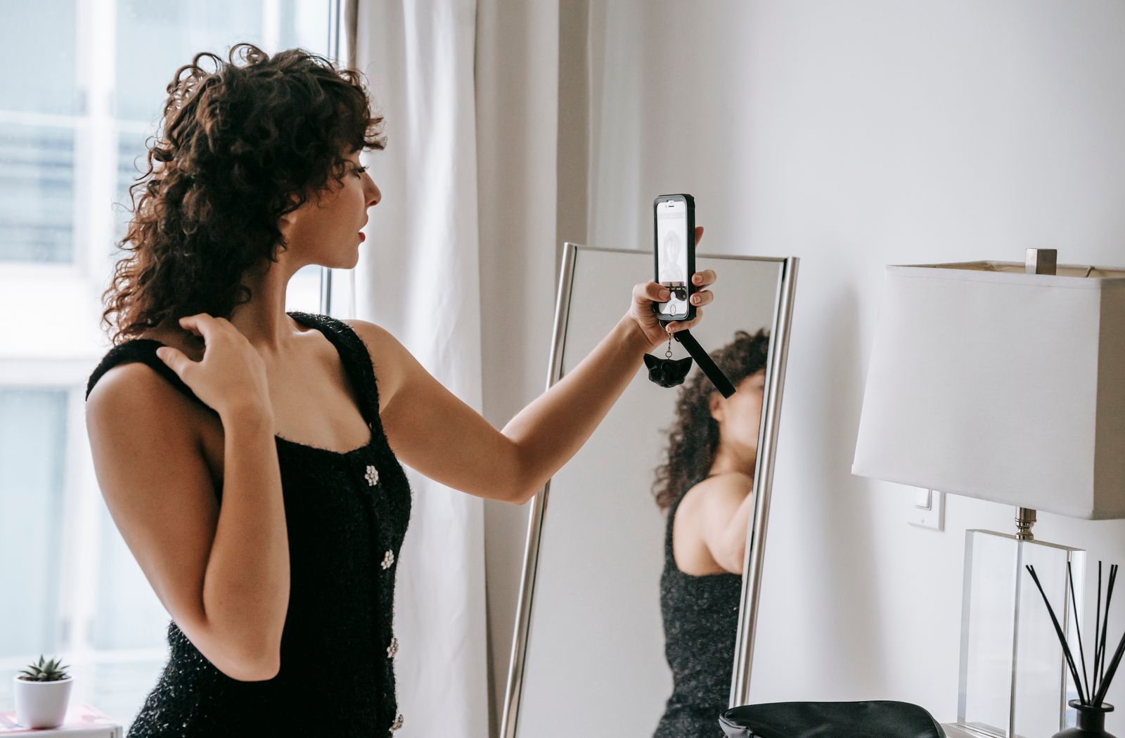Woman comparing her reflection with a smartphone selfie in front of a mirror