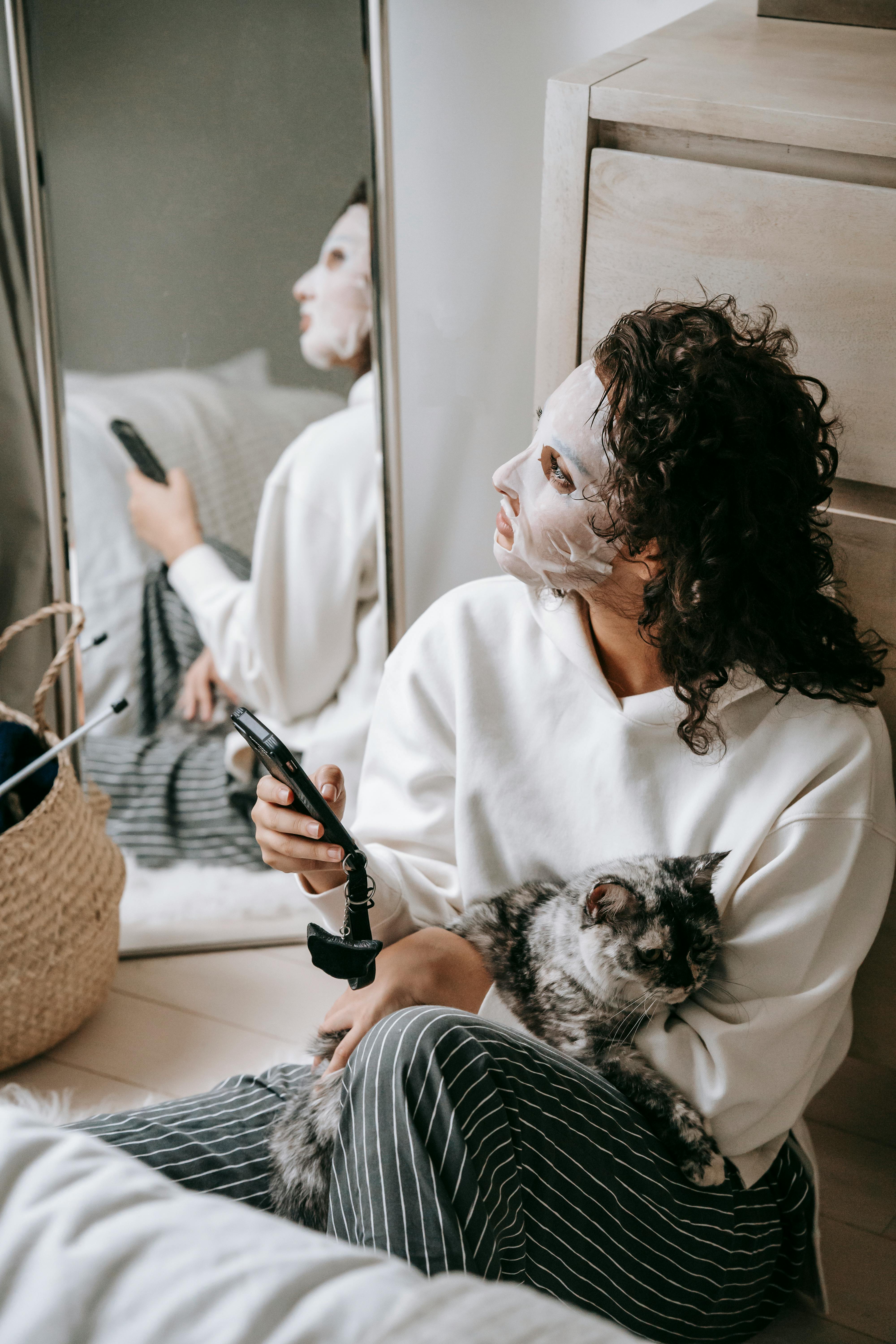 calm woman in facial mask with cat surfing cellphone