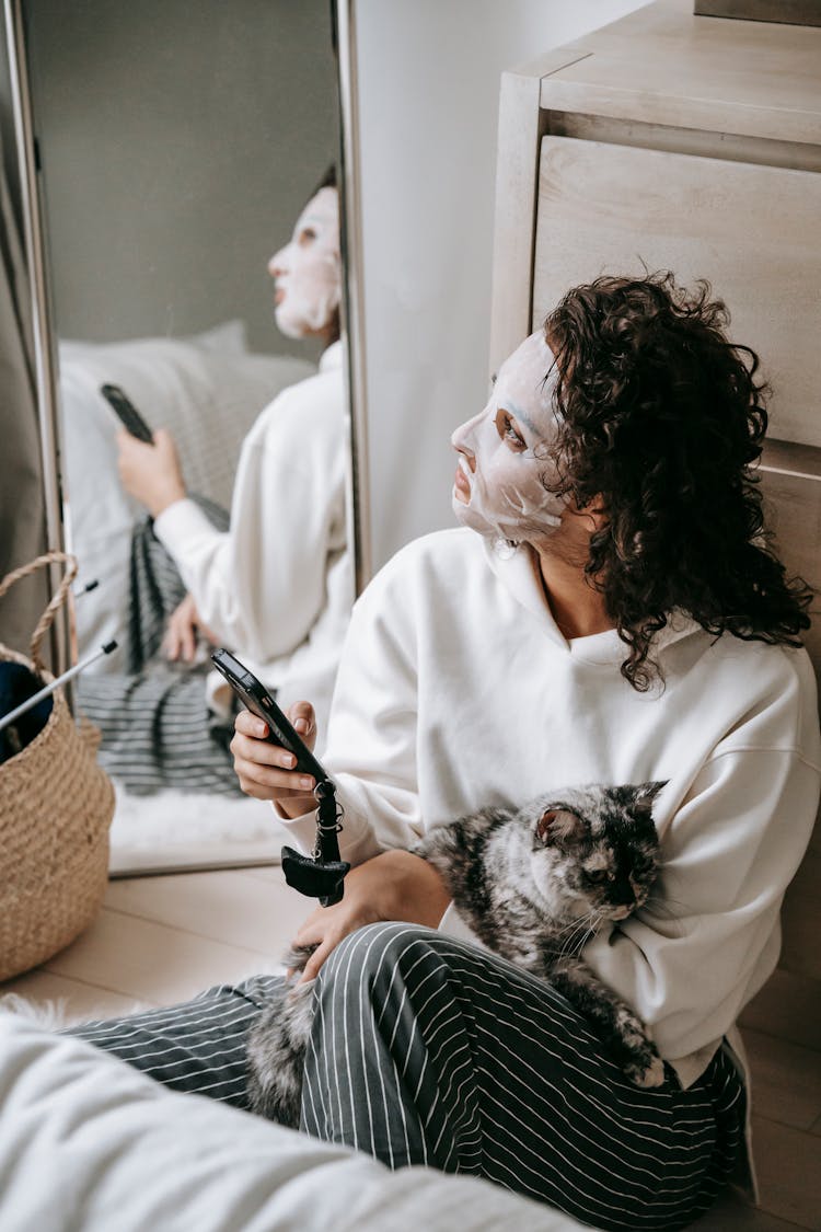 Calm Woman In Facial Mask With Cat Surfing Cellphone